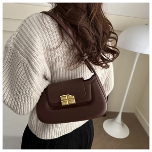 Detail der schokoladenbraunen Umhängetasche mit goldener Schnalle auf beigem Pullover