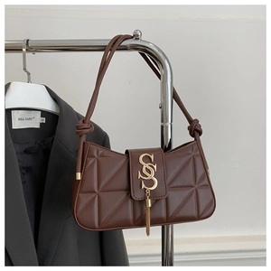 Detail of dark brown quilted underarm bag with gold metal buckle and tassel on grey blazer