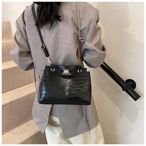 Modèle portant un sac à main noir motif crocodile avec fermoir doré sur un fond clair