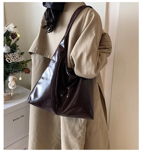 Side view of a large glossy dark brown tote bag worn on shoulder in a home setting