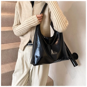 Detail of a black high-gloss tote bag with wide strap on a minimalist beige background