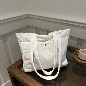 White quilted nylon tote bag with snap closure shown on a coffee table in a modern room
