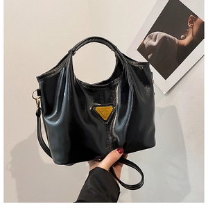 Detailed view of black patent leather tote bag with triangular logo and detachable strap