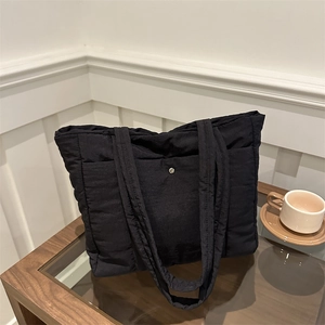 Minimalist black quilted tote bag with double shoulder straps and metal snap button