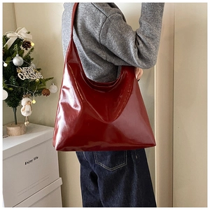 Detailed side view of a large burgundy leather tote bag with glossy finish on a model