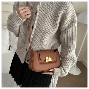 Brown leather square crossbody bag with gold metallic buckle on a knitted sweater background