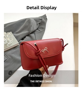 Detail of dark red crossbody bag featuring a metal bow buckle and knotted shoulder strap