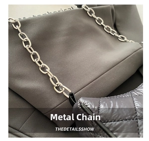 Detail of silver chain strap attached to dark grey quilted bag with satin texture