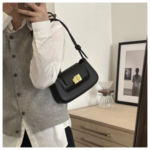 Detail of black leather shoulder bag featuring a golden geometric clasp and knotted strap
