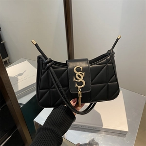 Chic black quilted shoulder bag with gold metal logo and tassel on white book background