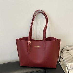 Grand sac cabas rétro bordeaux en cuir avec texte doré posé sur un banc en cuir
