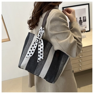 Detail of striped canvas tote bag with polka dot ribbon and brown leather handles