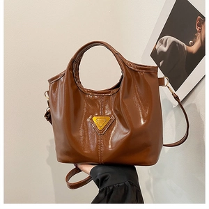 Detailed macro of vintage brown glossy leather tote bag with gold triangle logo hardware