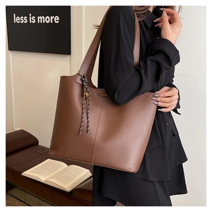 Brown faux leather tote bag with minimalist knot charm worn on shoulder