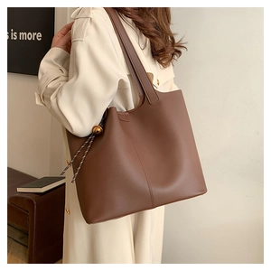 Detail view of large brown faux leather tote bag with gold ball charm on model