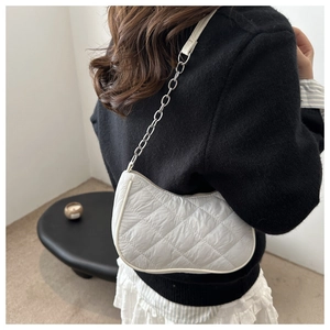 Detail of white quilted underarm bag with metal chain strap on model's shoulder