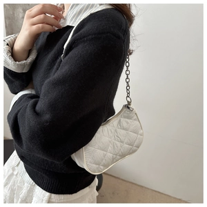 Close-up of a white quilted shoulder bag with silver chain strap worn by a model