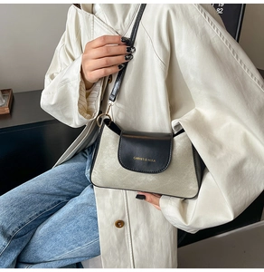 Dettaglio della patta nera opaca con logo dorato su una borsa a tracolla crema
