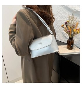 Detail of silver metallic underarm bag featuring a knot strap and metal bow accessory