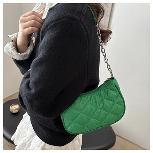 Close-up of green quilted shoulder bag with silver chain strap worn by a model