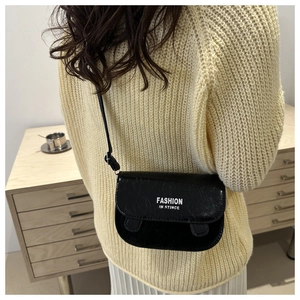Detail of black glossy saddle bag with white lettering on beige knitted sweater