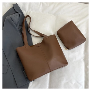 Brown leather tote bag set with matching pouch on white cloth next to a grey blazer