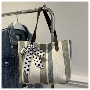 Detail of striped canvas tote with brown leather strap and polka dot bow charm