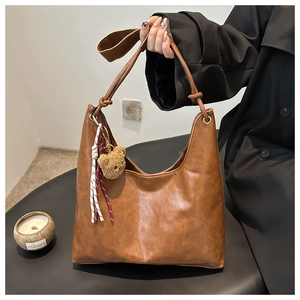 Détail du sac hobo en cuir marron vintage avec charm ours en peluche et pompon sur l'épaule