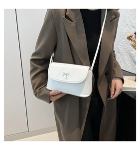 Détail de la boucle nœud argentée sur un sac bandoulière blanc porté avec un blazer