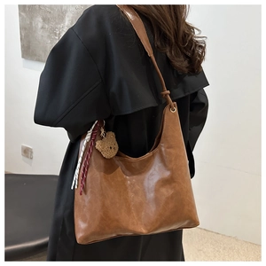 Détail d'un sac cabas en cuir marron avec charm ours et sangle tissée colorée