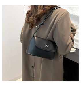 Détail du sac sous l'aisselle en cuir noir avec un nœud argenté sur la bandoulière