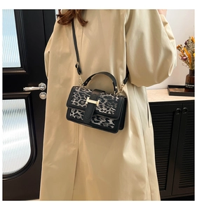 Detail of leopard print crossbody bag with gold buckle and black handle on coat