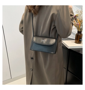 Detail view of mini black leather bag with silver bow buckle worn on the shoulder