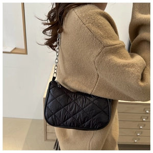 Detail of black quilted shoulder bag with silver chain strap and modern texture