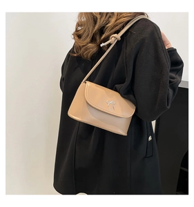 Detail view of beige bow-accented shoulder bag styled on a minimalist black coat