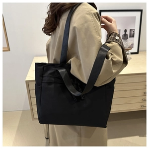 Close-up of black nylon tote bag with wide strap on shoulder of model in trench coat