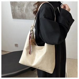 Modell trägt eine beige Einkaufstasche mit Bärenanhänger und rot karierter Schleife im Detail