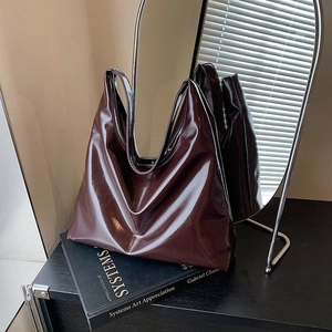 Glossy burgundy leather tote bag styled on an art book with cinematic shadow lighting