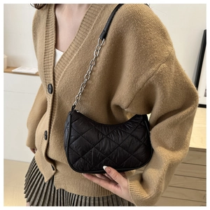 Detail of black quilted shoulder bag with silver chain strap shown with winter outfit