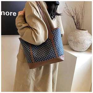 Detail of blue geometric tote bag with brown leather straps worn over the shoulder