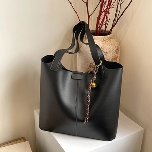 Minimalist black leather tote bag with a decorative bell pendant on a geometric pedestal