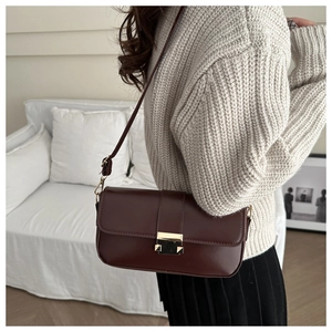 Detail of burgundy vintage crossbody bag with gold buckle on a model's shoulder
