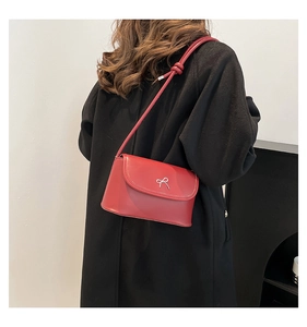 Détail d'un sac à bandoulière rouge avec nœud argenté porté sur un long manteau noir d'hiver