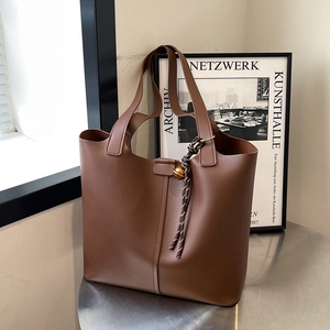Large dark brown leather tote bag with braided charm on silver desk, modern minimalist style