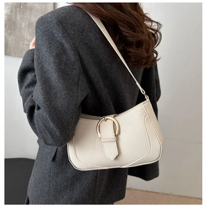 Detailed view of cream leather shoulder bag with gold buckle on model in natural light