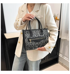 Detail view of leopard print tote bag with black leather handle and front zipper pocket