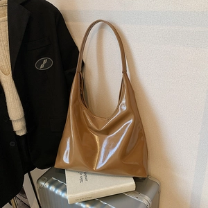 Brown patent leather hobo shoulder bag with glossy finish on a silver suitcase