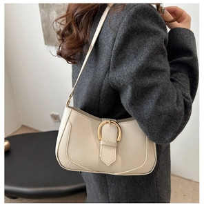 Detail of off-white leather shoulder bag with golden horseshoe buckle on tweed coat
