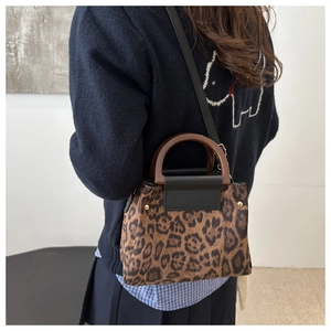 Detail of leopard print crossbody bag with wooden handle and gold rivet accents