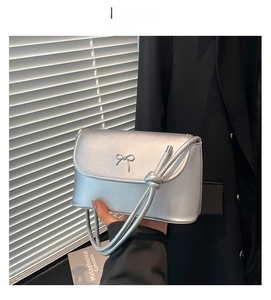 Detail of silver metallic shoulder bag with decorative bow buckle and sleek finish